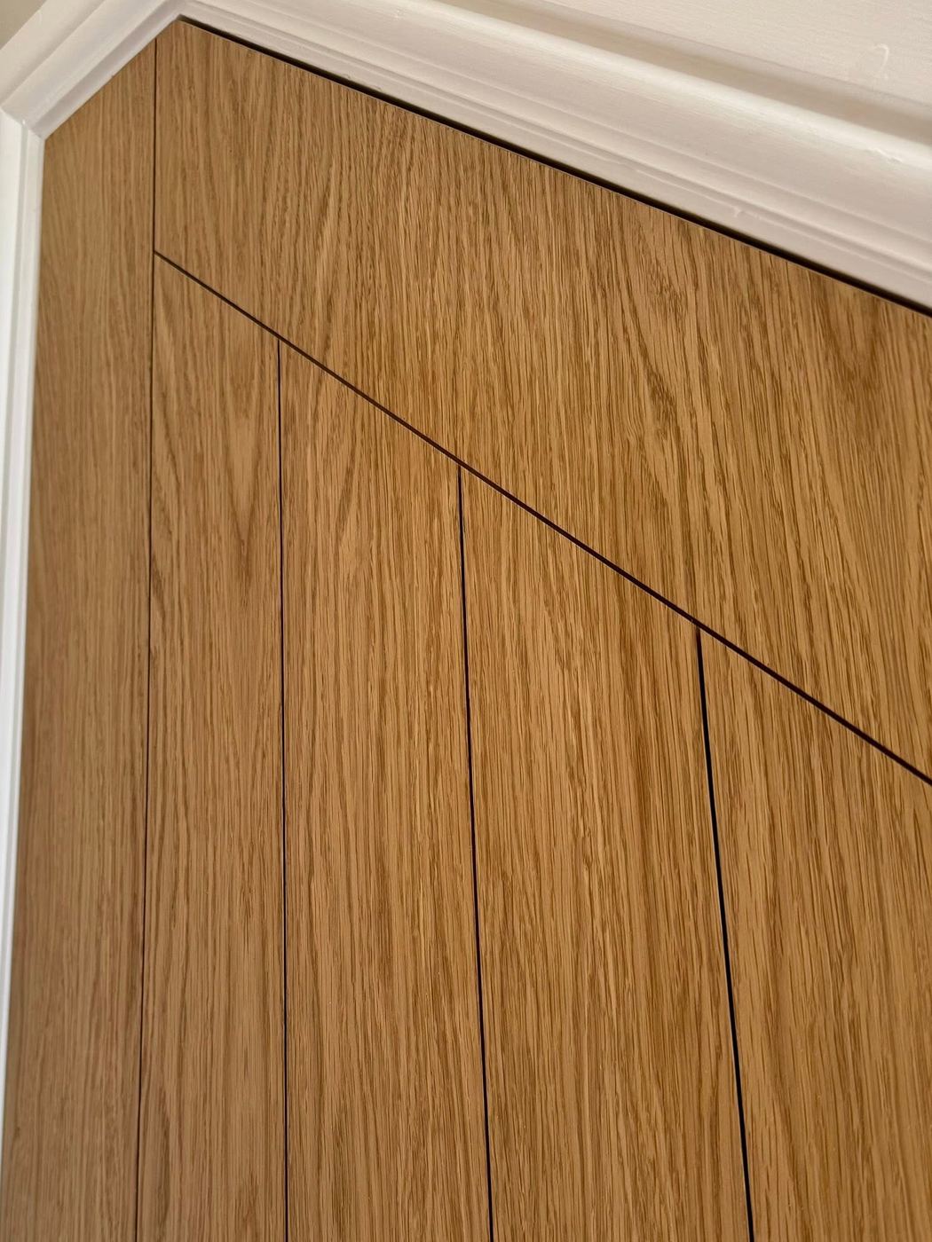 Close crop of oak-faced wardrobe doors showing continuous grain running across the shadow gaps