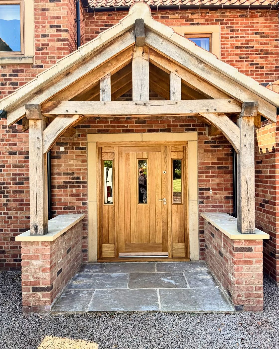 Green oak porch canopy with pegged trusses over a solid oak entrance door on a red brick house