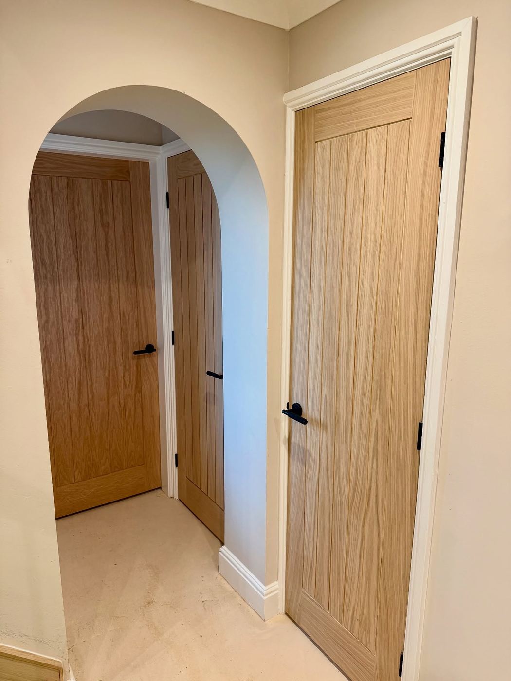 Solid oak tongue and groove doors with black ironmongery beside a plastered arched opening