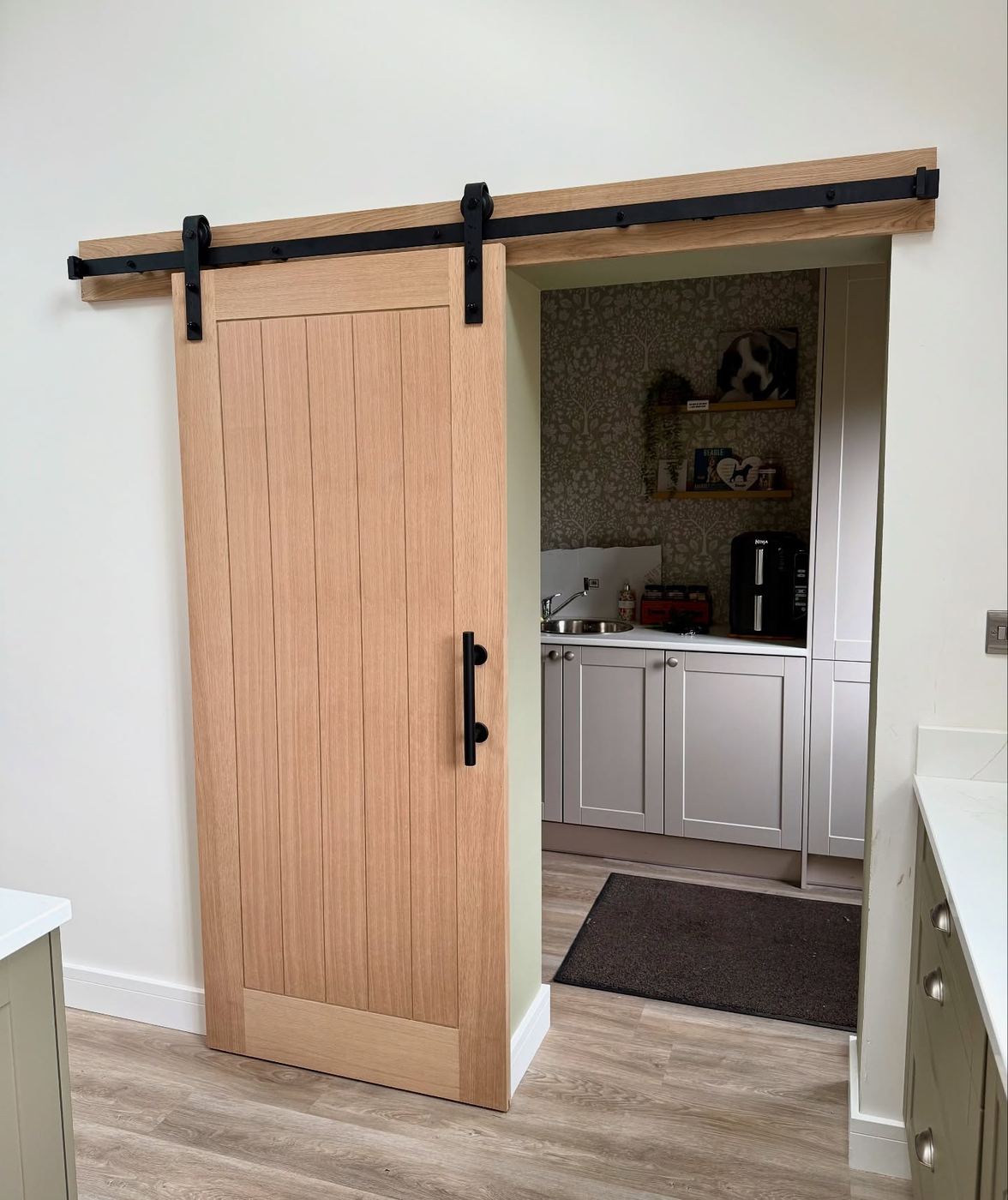 Oak barn-style sliding door on a black top track, slid open onto a fitted utility room