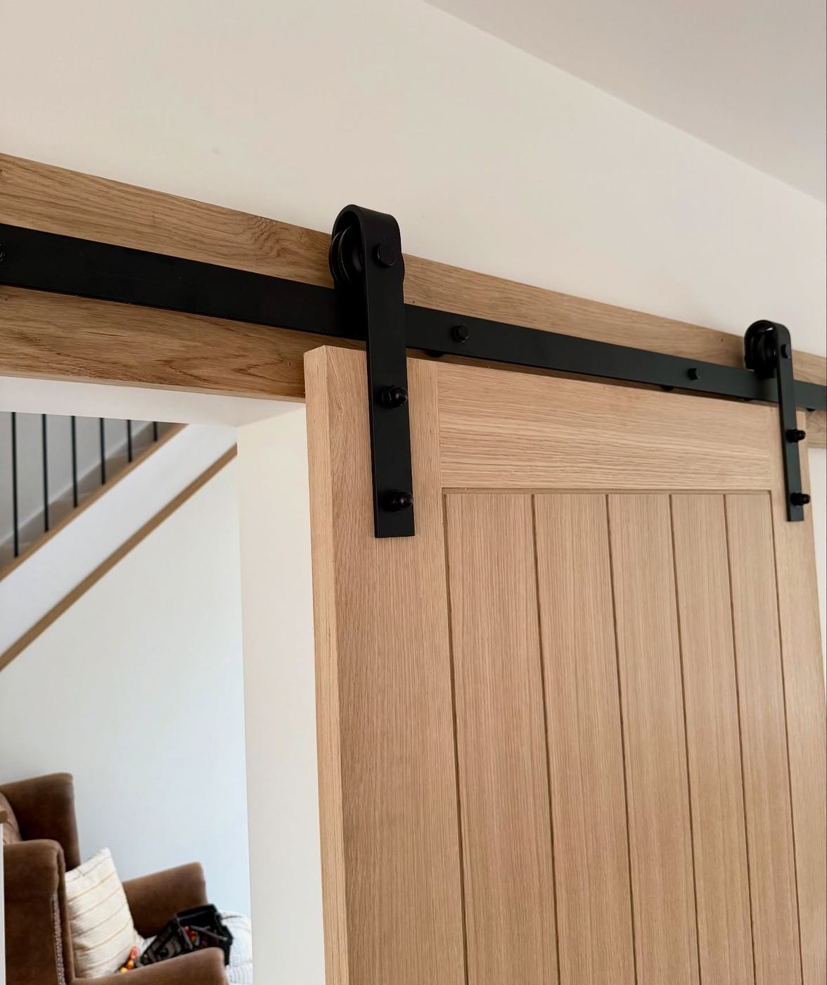 Black sliding barn door track and hanger bolted to a solid oak header above an oak door