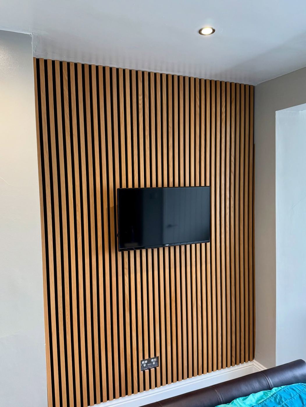 Full height oak slatted acoustic wall panelling with a wall-mounted television set into it