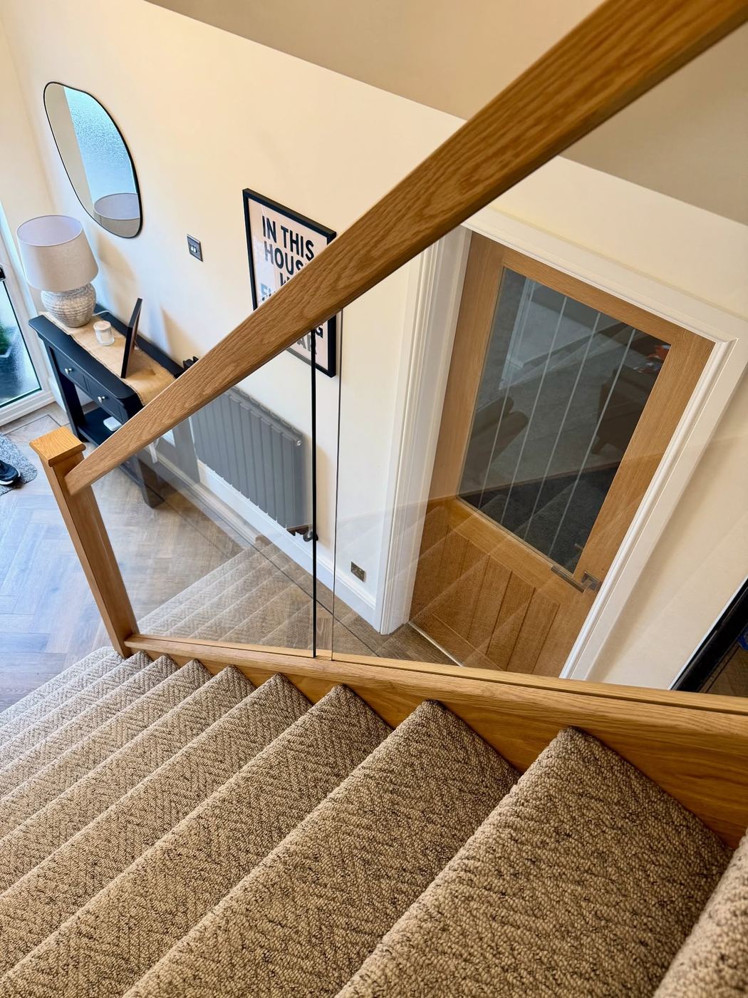 Oak staircase with a frameless glass balustrade, seen from the landing above