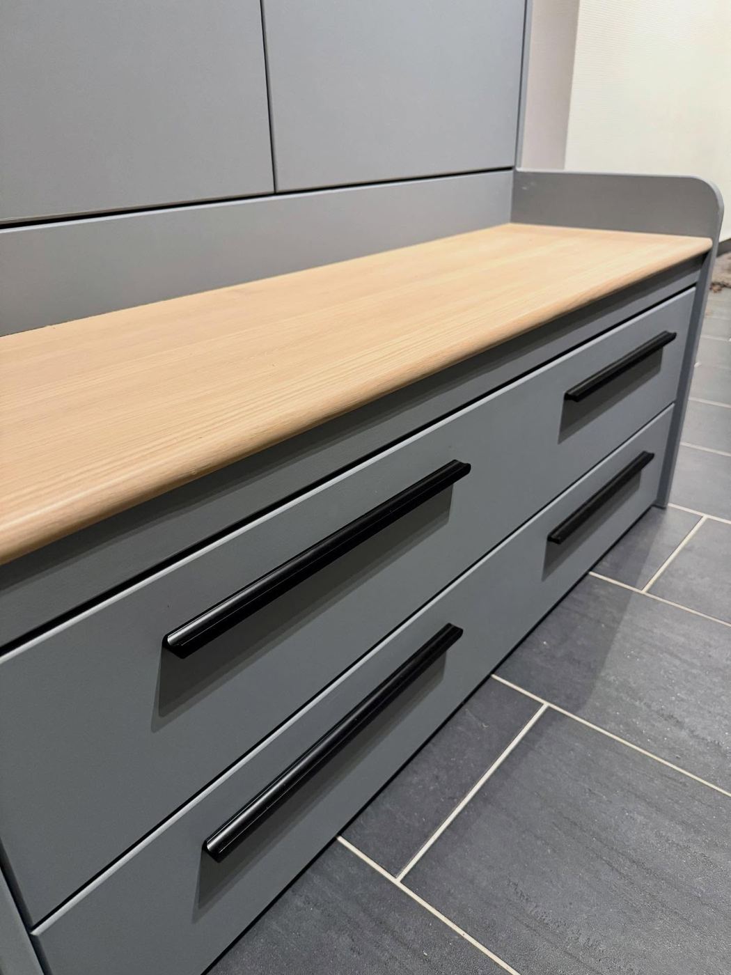 Graphite grey fitted drawers with long black handles beneath a solid oak seat top