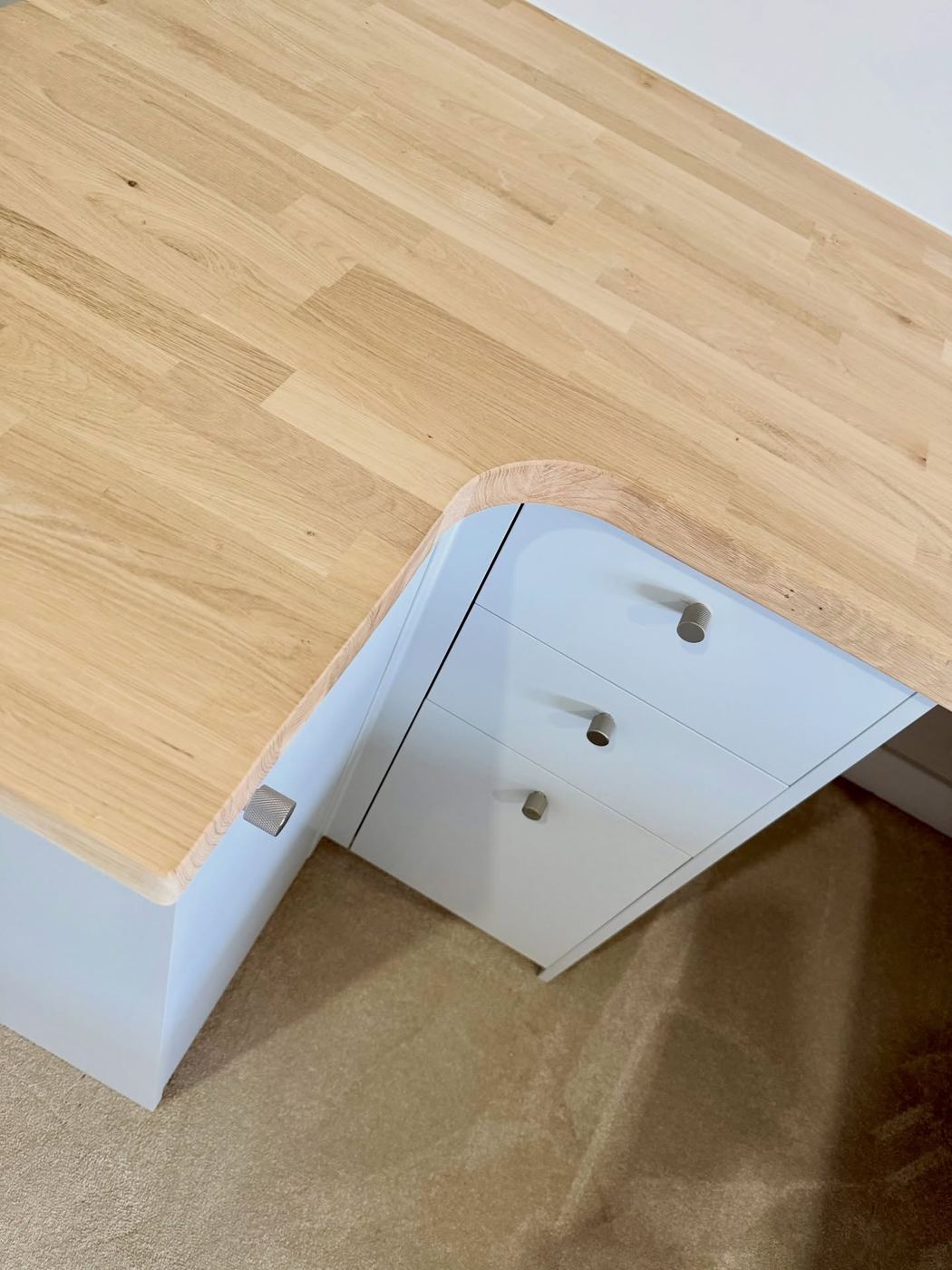 Detail of a solid oak worktop turning a rounded external corner above cream drawer fronts