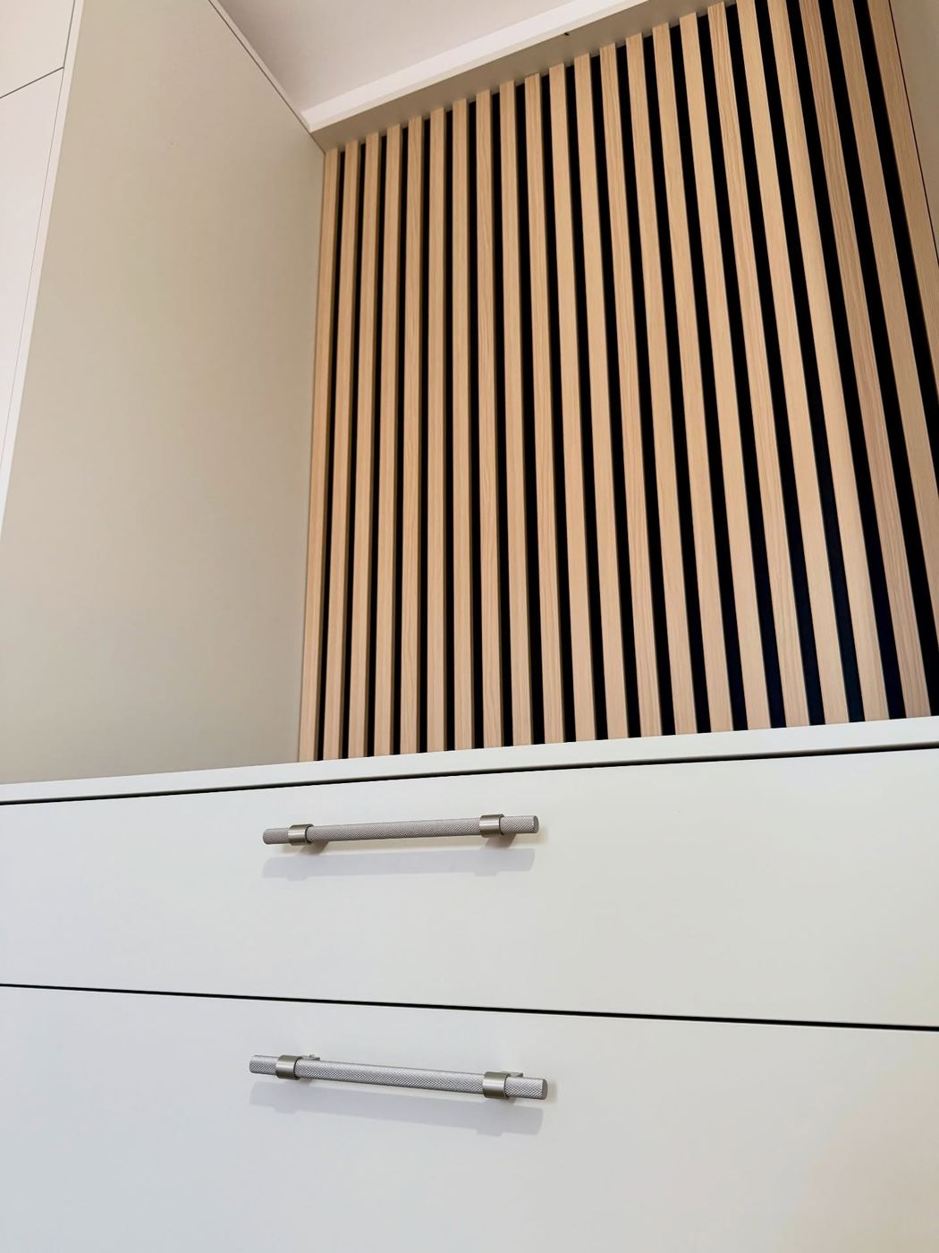 Handleless cream fitted drawers below a recessed oak slatted panel